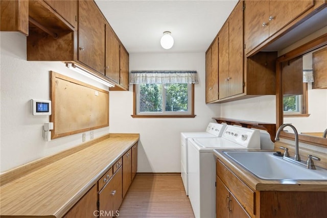 laundry area with washer and dryer, cabinet space, light wood-type flooring, and a sink