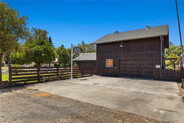 view of home's exterior with roof with shingles, fence, and a detached garage
