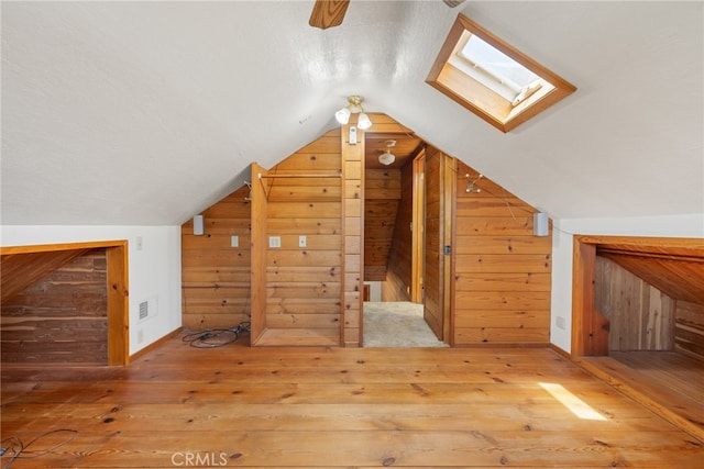 bonus room featuring wood-type flooring, wood walls, and vaulted ceiling with skylight