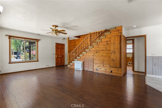 unfurnished living room with wooden walls, ceiling fan, and dark wood-type flooring