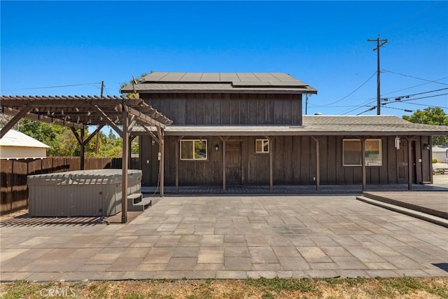 back of property with a hot tub, fence, a patio, a pergola, and solar panels