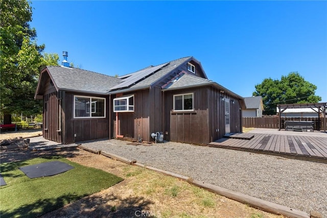 exterior space featuring a wooden deck, a shingled roof, solar panels, and a jacuzzi