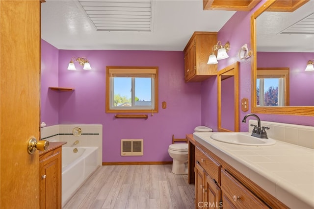 bathroom with heating unit, hardwood / wood-style flooring, a tub, vanity, and toilet