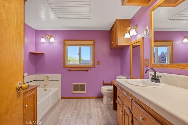 bathroom featuring heating unit, toilet, wood finished floors, a bath, and vanity