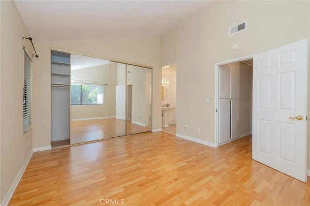 unfurnished bedroom with ensuite bath, a closet, light hardwood / wood-style floors, and lofted ceiling