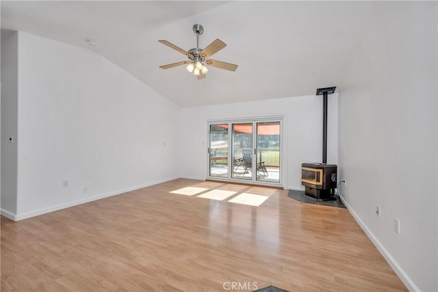 unfurnished living room with lofted ceiling, ceiling fan, a wood stove, and light hardwood / wood-style flooring