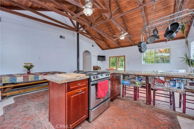 kitchen featuring ceiling fan, a center island, beamed ceiling, high vaulted ceiling, and stainless steel stove