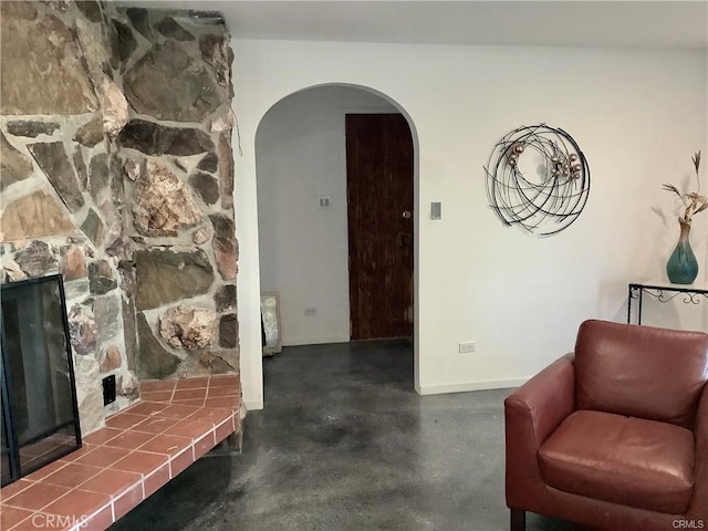 sitting room with arched walkways, a fireplace, finished concrete flooring, and baseboards