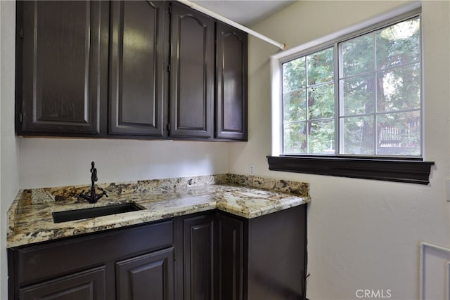 kitchen featuring light stone countertops, sink, and dark brown cabinets