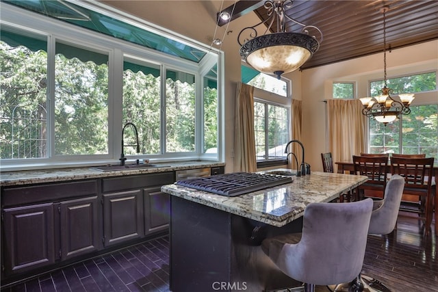 kitchen with light stone countertops, sink, pendant lighting, a notable chandelier, and a center island