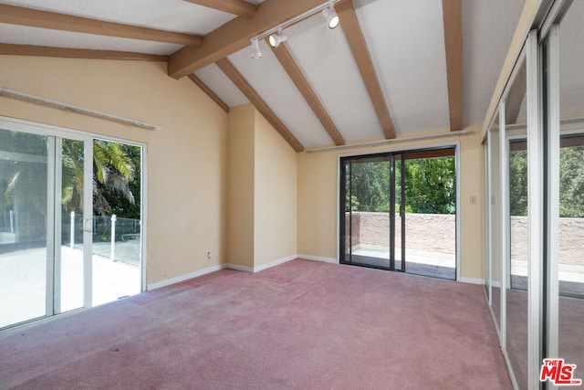 unfurnished room with lofted ceiling with beams, a wealth of natural light, track lighting, and carpet floors