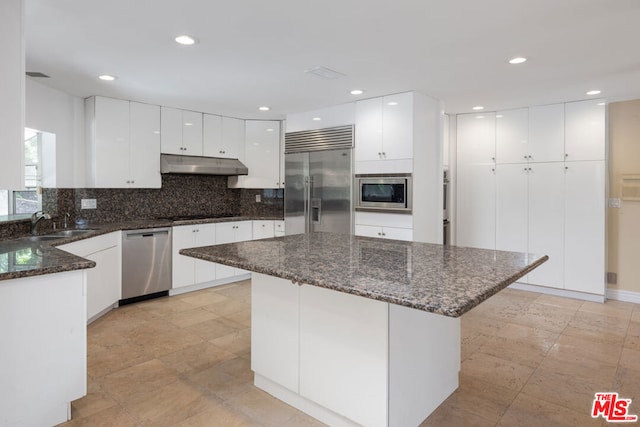 kitchen featuring white cabinets, sink, built in appliances, dark stone counters, and decorative backsplash