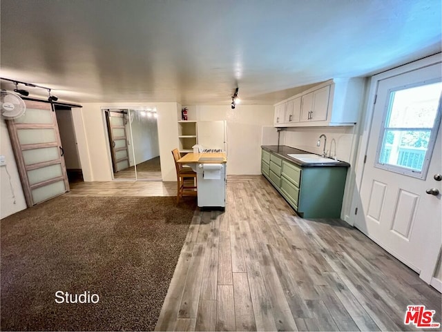 kitchen with hardwood / wood-style flooring, green cabinets, sink, a barn door, and white cabinets