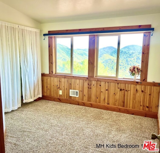 carpeted spare room with lofted ceiling, a mountain view, and wood walls