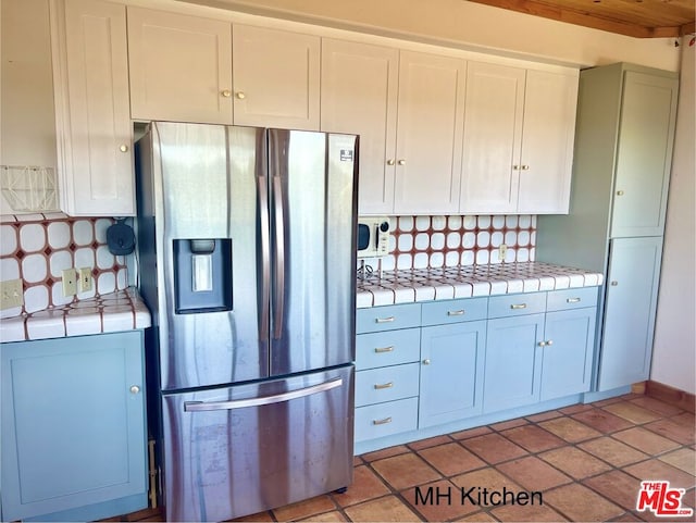 kitchen with tile countertops, stainless steel fridge, light tile patterned floors, and backsplash