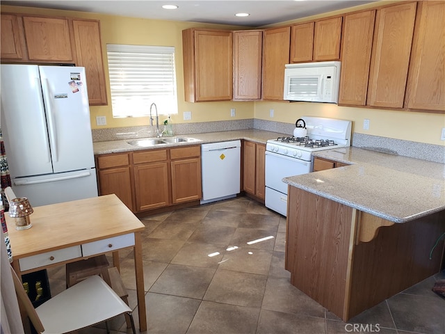 kitchen with dark tile patterned floors, white appliances, kitchen peninsula, and sink