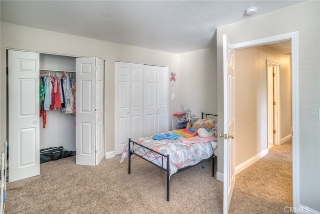 bedroom featuring multiple closets, a textured ceiling, and light colored carpet