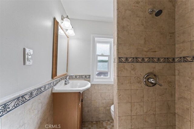 bathroom with a tile shower, vanity, toilet, and tile walls