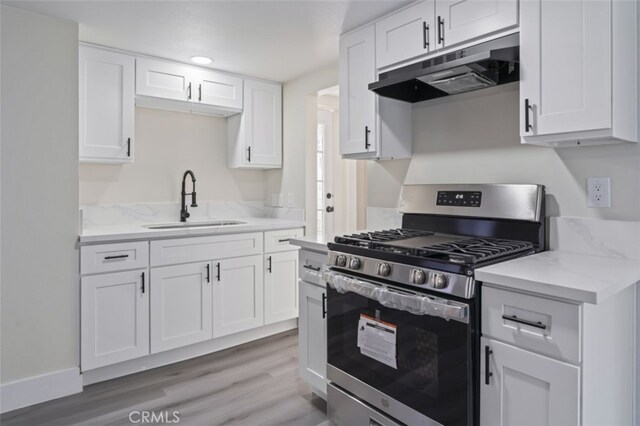 kitchen with light stone counters, gas range, sink, light hardwood / wood-style flooring, and white cabinets