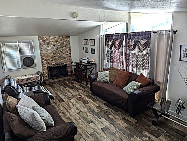 living room featuring lofted ceiling, a textured ceiling, dark wood-type flooring, and a stone fireplace