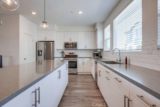 kitchen with hanging light fixtures, white cabinetry, wood-type flooring, and stainless steel appliances