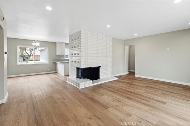 unfurnished living room featuring light hardwood / wood-style floors, a multi sided fireplace, and an inviting chandelier