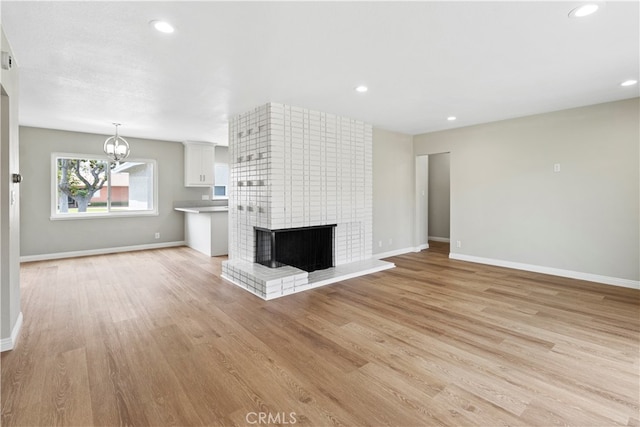 unfurnished living room with an inviting chandelier, light wood-type flooring, and a fireplace