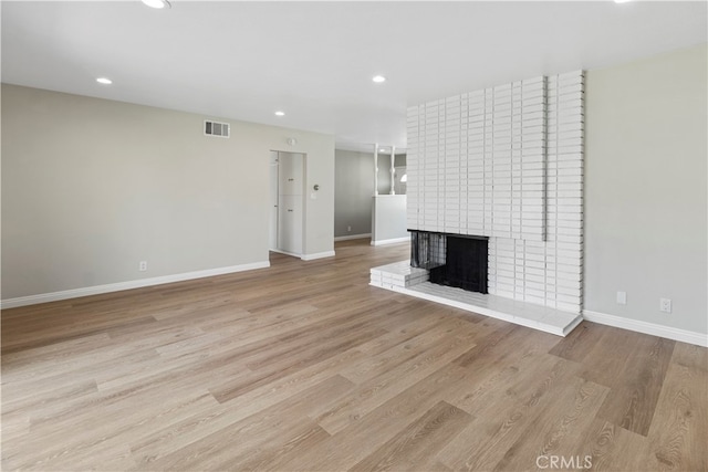 unfurnished living room featuring light hardwood / wood-style flooring and a brick fireplace