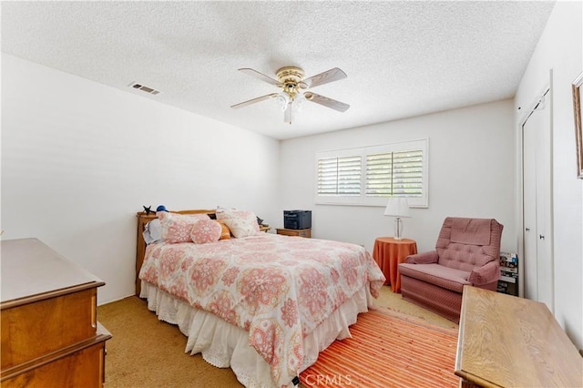 bedroom with light carpet, visible vents, ceiling fan, a textured ceiling, and a closet