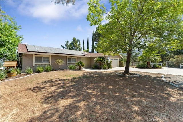 ranch-style home with stucco siding, solar panels, concrete driveway, an attached garage, and fence