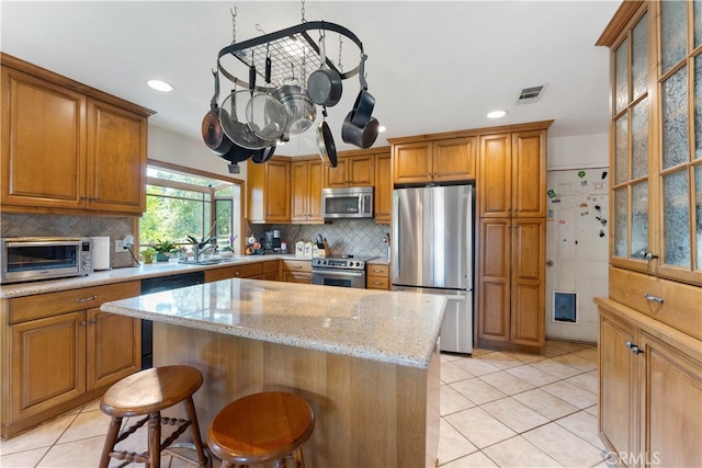 kitchen with appliances with stainless steel finishes, a center island, a kitchen breakfast bar, light stone counters, and light tile patterned floors