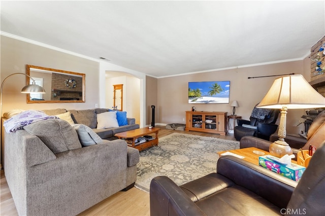 living room featuring crown molding, a brick fireplace, and light wood-type flooring