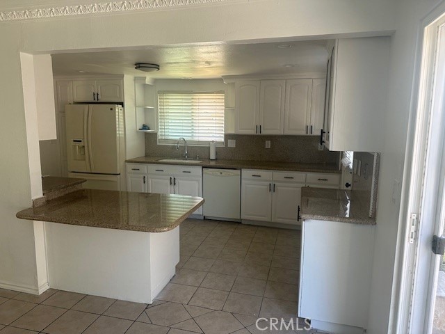 kitchen with kitchen peninsula, white cabinets, light tile patterned flooring, sink, and white appliances