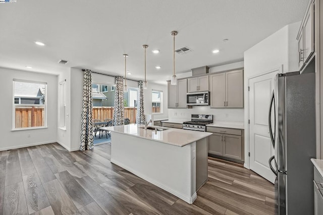 kitchen featuring appliances with stainless steel finishes, a center island with sink, dark hardwood / wood-style flooring, and a wealth of natural light