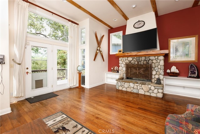 unfurnished living room with a wealth of natural light, beamed ceiling, a stone fireplace, and hardwood / wood-style flooring