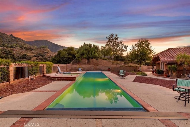 pool at dusk with a mountain view and a patio area