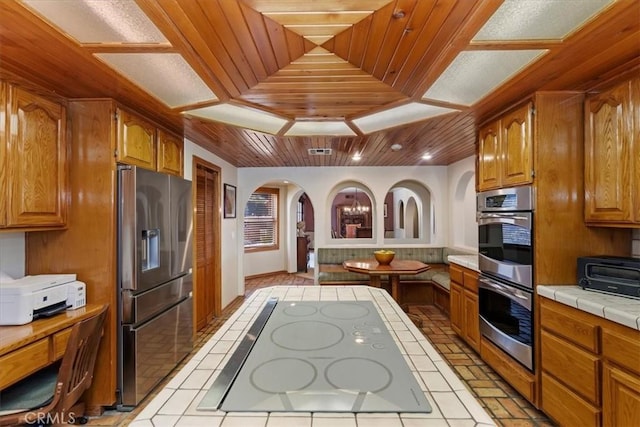 kitchen with a raised ceiling, tile countertops, wood ceiling, and appliances with stainless steel finishes