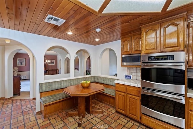 kitchen featuring decorative backsplash, breakfast area, wood ceiling, stainless steel appliances, and tile countertops