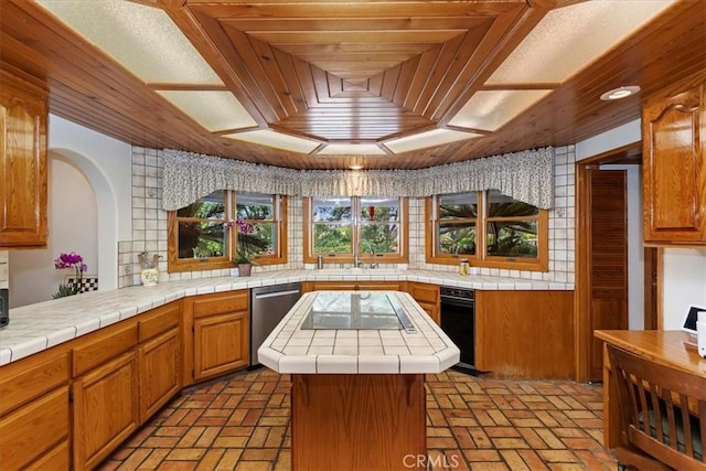 kitchen with stainless steel dishwasher, black electric cooktop, sink, a center island, and tile counters