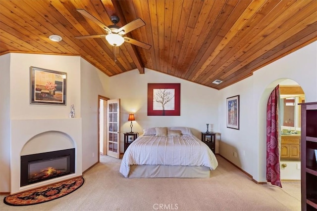 carpeted bedroom with ceiling fan, lofted ceiling with beams, wood ceiling, and ensuite bath