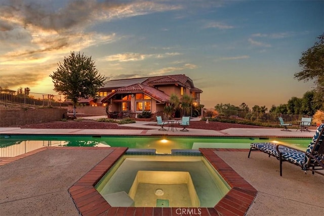 pool at dusk featuring a patio area and an in ground hot tub