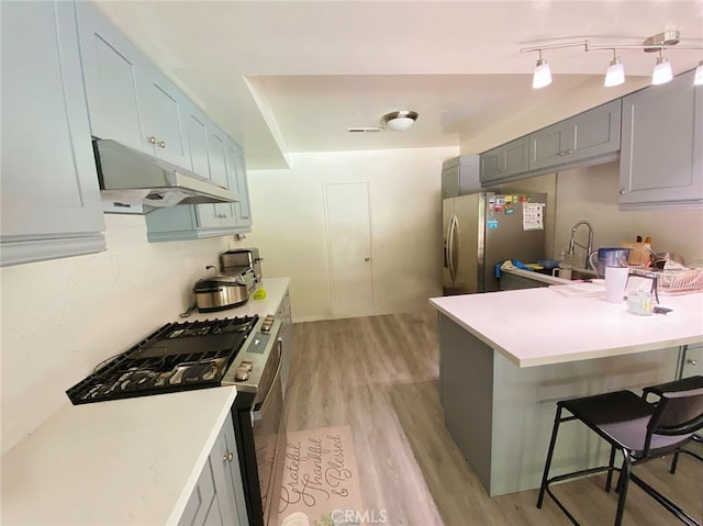 kitchen featuring gray cabinetry, appliances with stainless steel finishes, light wood-type flooring, a kitchen bar, and kitchen peninsula