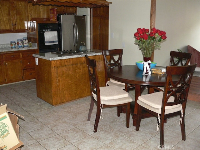 kitchen featuring black oven, stainless steel fridge, gas stovetop, and light tile patterned flooring