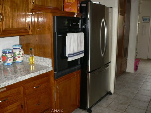 kitchen with stainless steel refrigerator, light stone countertops, light tile patterned floors, and black oven