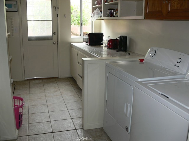 clothes washing area with light tile patterned floors, cabinets, and independent washer and dryer