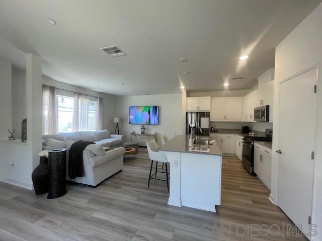 kitchen with white cabinets, appliances with stainless steel finishes, light hardwood / wood-style flooring, sink, and a center island with sink