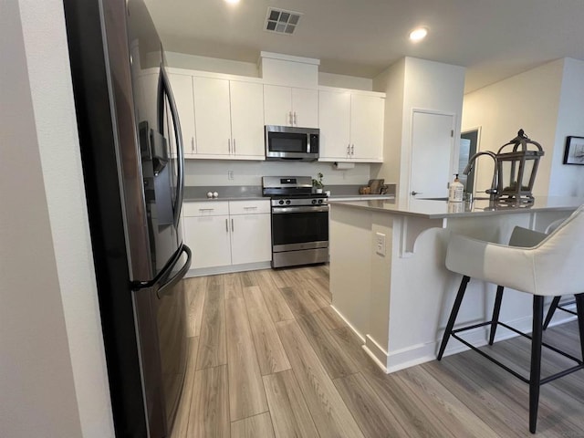 kitchen with white cabinets, a kitchen breakfast bar, stainless steel appliances, and light hardwood / wood-style floors