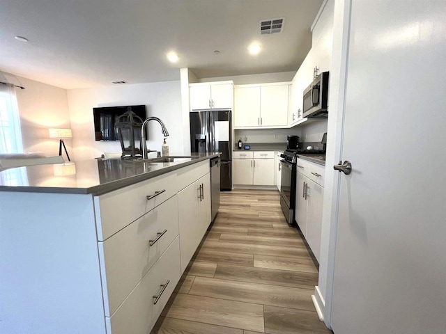 kitchen featuring light hardwood / wood-style floors, a center island with sink, sink, appliances with stainless steel finishes, and white cabinets