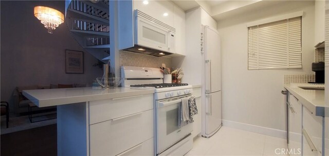 kitchen featuring white cabinetry, an inviting chandelier, white appliances, decorative backsplash, and light tile patterned floors