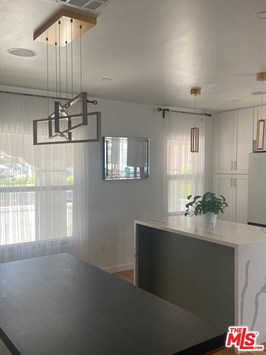 kitchen with a wealth of natural light, pendant lighting, fridge, and white cabinets